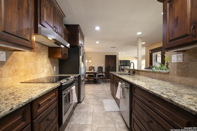 kitchen featuring light tile patterned floors, light stone counters, a sink, under cabinet range hood, and appliances with stainless steel finishes