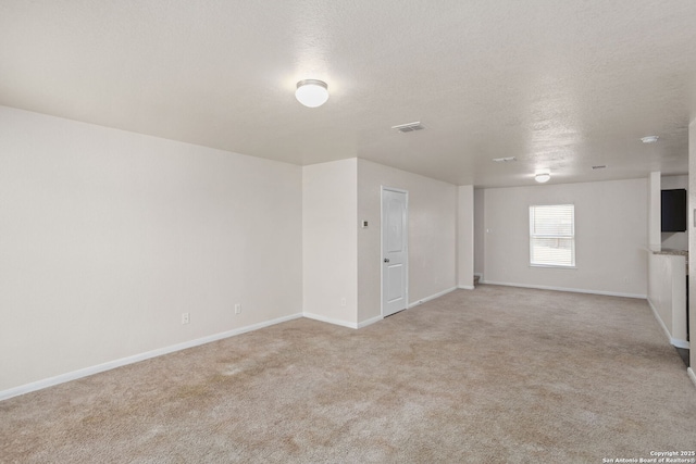 spare room featuring visible vents, light colored carpet, a textured ceiling, and baseboards