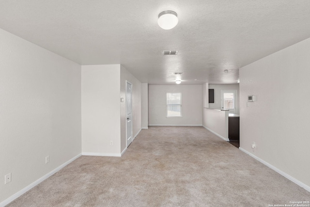 empty room with light carpet, visible vents, a textured ceiling, and baseboards