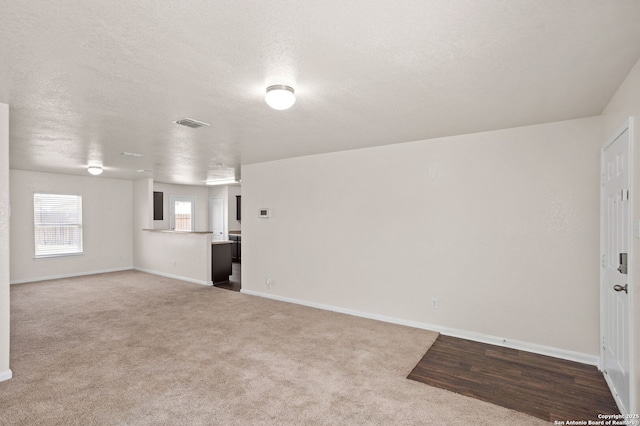 empty room with carpet flooring, visible vents, a textured ceiling, and baseboards