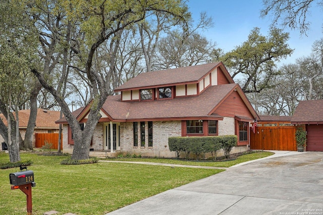 tudor-style house featuring a front lawn, fence, brick siding, and roof with shingles