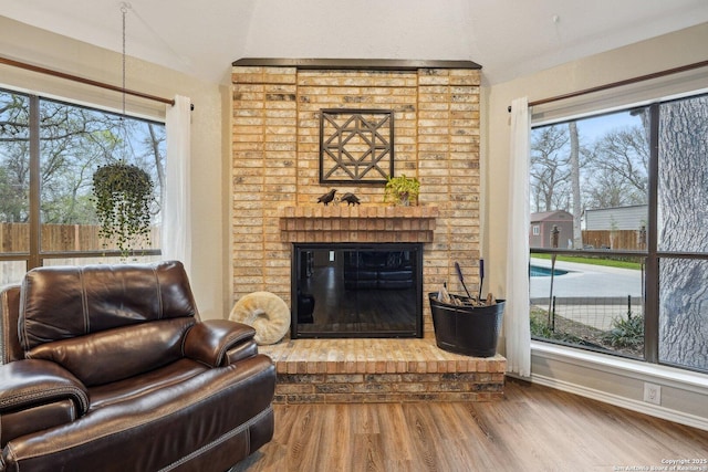 living area with a fireplace, lofted ceiling, baseboards, and wood finished floors