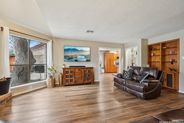 living room with visible vents, baseboards, a textured ceiling, and wood finished floors