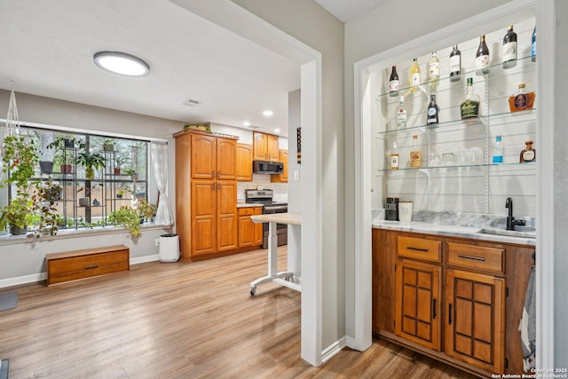 bar featuring stainless steel electric range oven, decorative backsplash, wet bar, light wood-style floors, and a sink