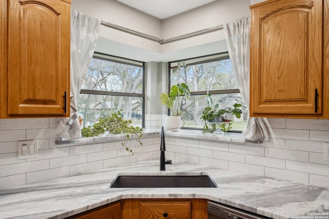 kitchen with light stone counters, decorative backsplash, brown cabinetry, and a sink