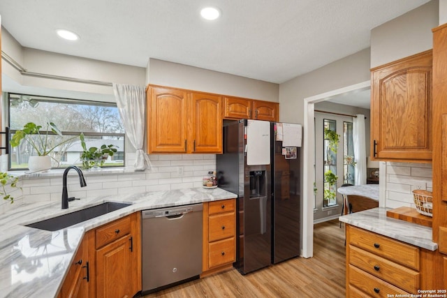 kitchen featuring a sink, light wood-type flooring, light stone counters, and appliances with stainless steel finishes