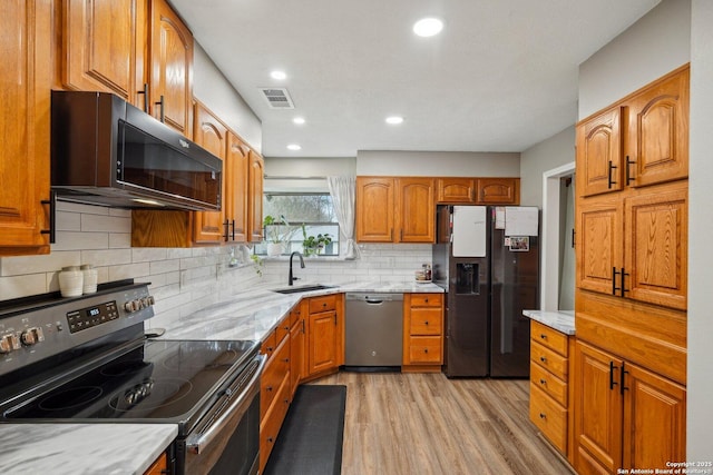 kitchen featuring light wood finished floors, visible vents, backsplash, black appliances, and a sink