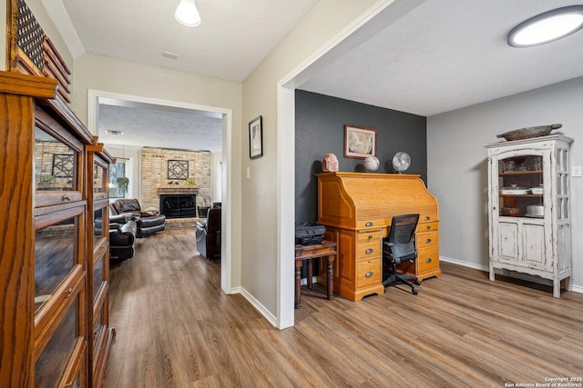 office space with a brick fireplace, a textured ceiling, baseboards, and wood finished floors