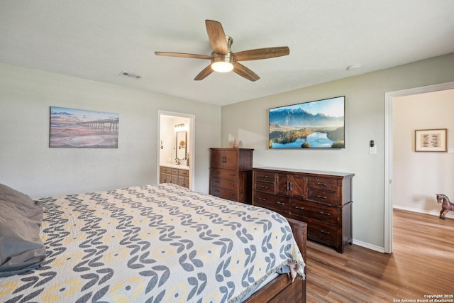 bedroom with visible vents, ensuite bathroom, a ceiling fan, wood finished floors, and baseboards