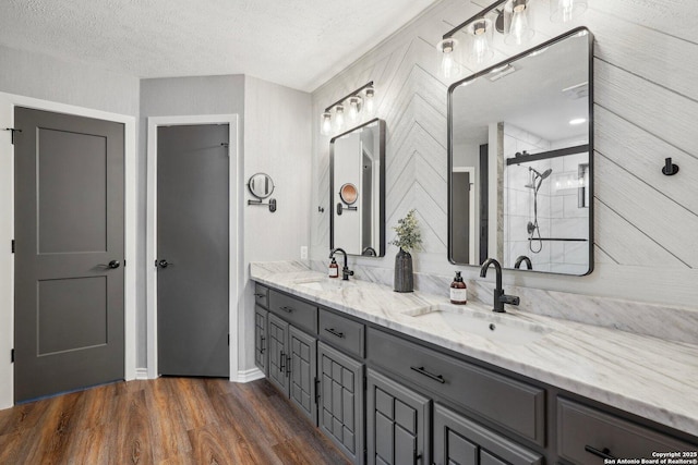 full bath with double vanity, a shower stall, wood finished floors, and a sink