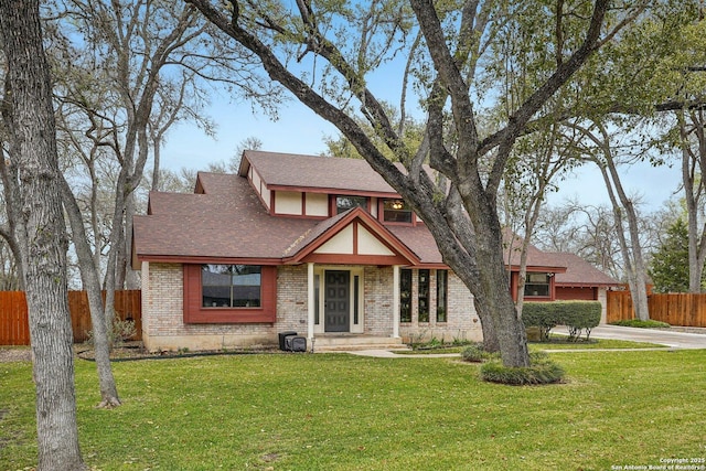 english style home featuring a front yard, fence, brick siding, and a shingled roof