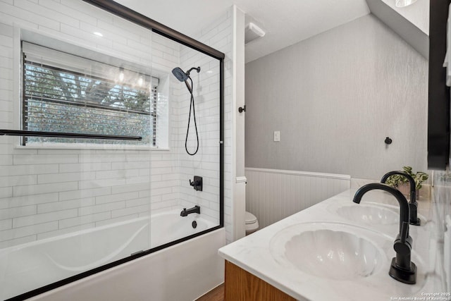 full bathroom featuring a wainscoted wall, toilet, a sink, double vanity, and bath / shower combo with glass door