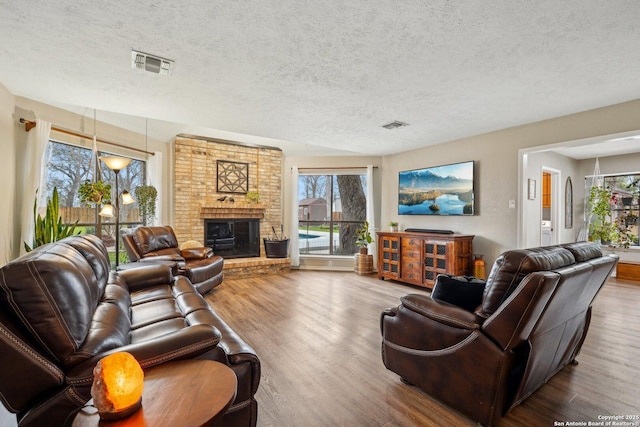 living room with visible vents, a textured ceiling, a brick fireplace, and wood finished floors