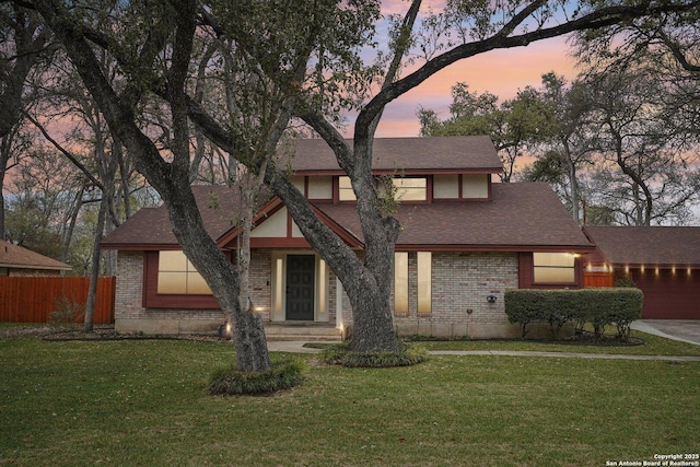 tudor house featuring brick siding, fence, a lawn, and roof with shingles