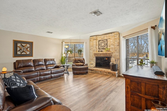 living area featuring a fireplace, wood finished floors, visible vents, and a wealth of natural light