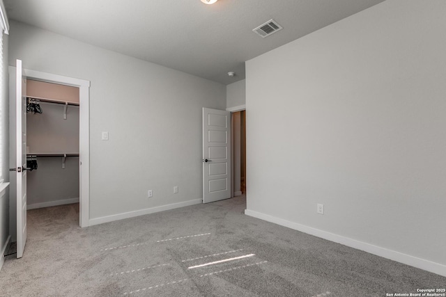 unfurnished bedroom with a spacious closet, visible vents, baseboards, carpet flooring, and a closet