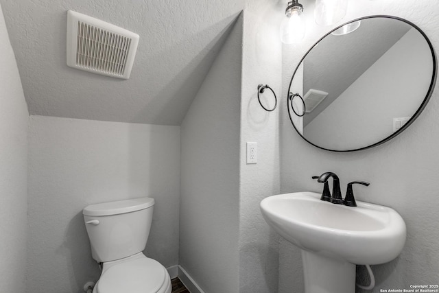 half bath with visible vents, baseboards, toilet, lofted ceiling, and a sink