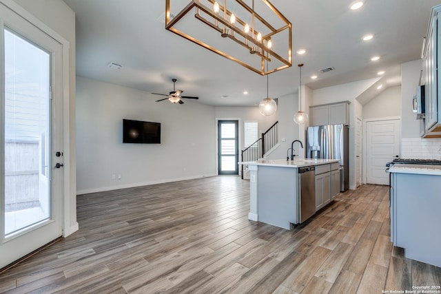 kitchen featuring light wood finished floors, gray cabinetry, light countertops, appliances with stainless steel finishes, and open floor plan