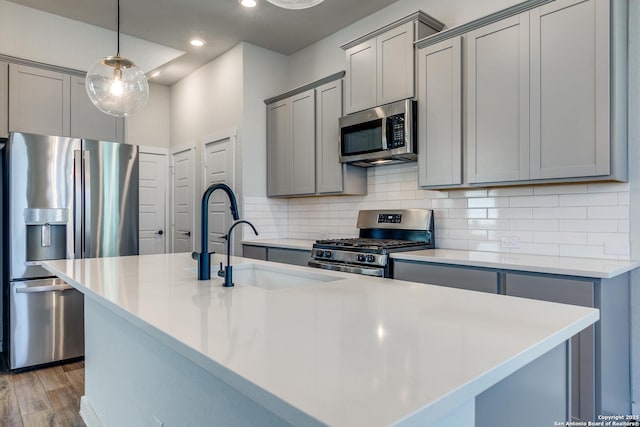 kitchen with light wood-style flooring, gray cabinets, an island with sink, stainless steel appliances, and decorative backsplash