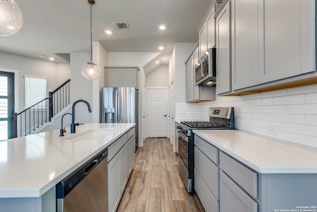 kitchen featuring tasteful backsplash, visible vents, gray cabinets, stainless steel appliances, and a sink