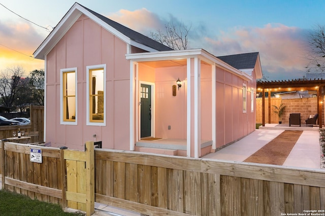 back of house at dusk with a patio, fence, and board and batten siding