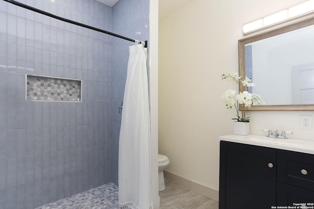 full bath featuring baseboards, tiled shower, toilet, and vanity