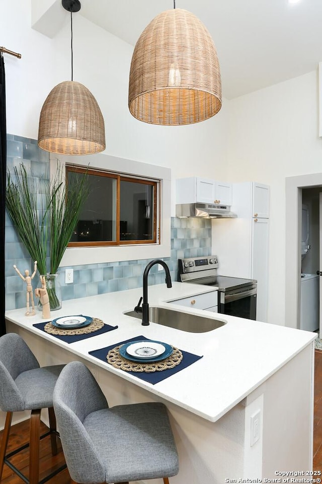 kitchen with a sink, stainless steel range with electric stovetop, under cabinet range hood, decorative light fixtures, and backsplash