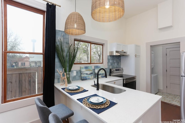 kitchen with stacked washer / dryer, under cabinet range hood, light countertops, appliances with stainless steel finishes, and a sink