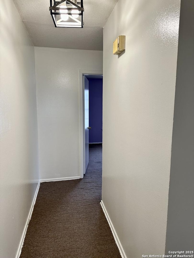 hallway with baseboards, dark carpet, and a textured ceiling