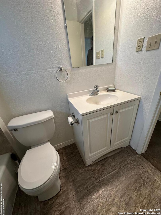 bathroom featuring toilet, vanity, and a textured wall