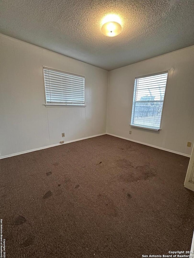 spare room featuring baseboards, a textured ceiling, and dark carpet