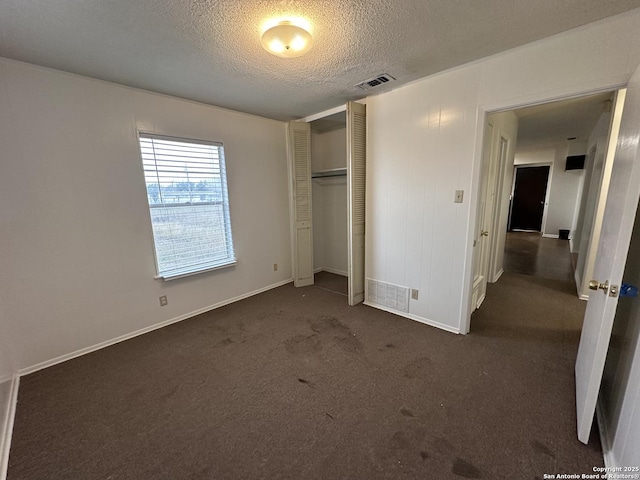 unfurnished bedroom with visible vents, a textured ceiling, dark carpet, a closet, and baseboards