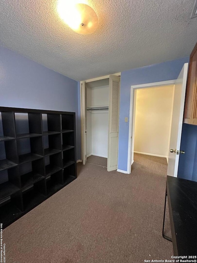 unfurnished bedroom featuring a closet, dark carpet, a textured ceiling, and baseboards