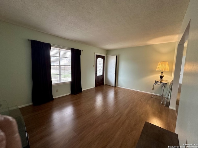 unfurnished living room featuring dark wood-style floors, a textured ceiling, and baseboards