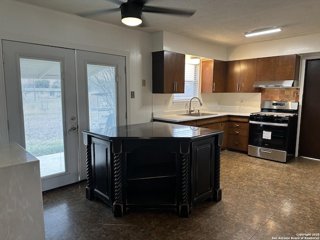 kitchen with a ceiling fan, stainless steel range with gas stovetop, a sink, under cabinet range hood, and a textured ceiling