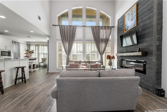 living area with a glass covered fireplace, dark wood-style floors, recessed lighting, a high ceiling, and baseboards