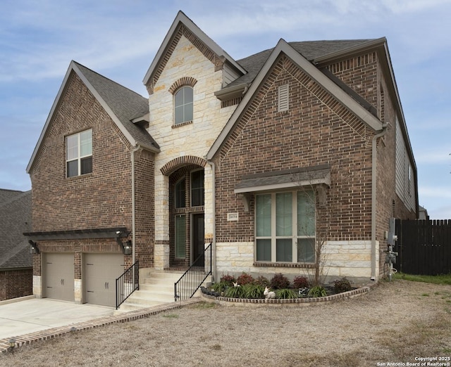 french country inspired facade featuring fence, driveway, a garage, stone siding, and brick siding