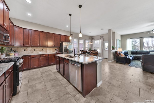 kitchen with light stone countertops, a sink, appliances with stainless steel finishes, open floor plan, and backsplash