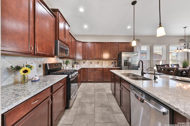 kitchen with a sink, light stone counters, appliances with stainless steel finishes, and hanging light fixtures