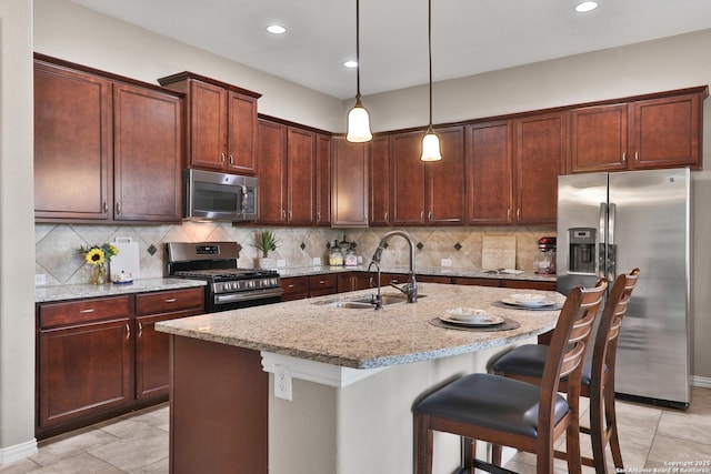 kitchen with light stone counters, a sink, appliances with stainless steel finishes, a kitchen breakfast bar, and tasteful backsplash