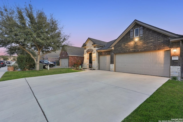 view of front of property featuring brick siding, concrete driveway, a lawn, stone siding, and an attached garage