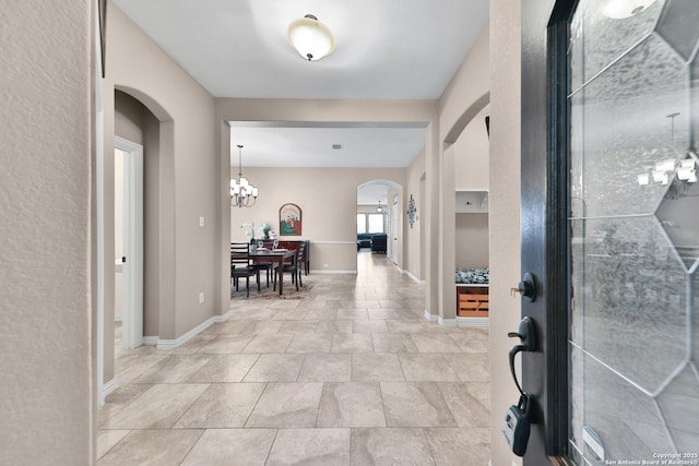 entrance foyer featuring baseboards, arched walkways, and a chandelier