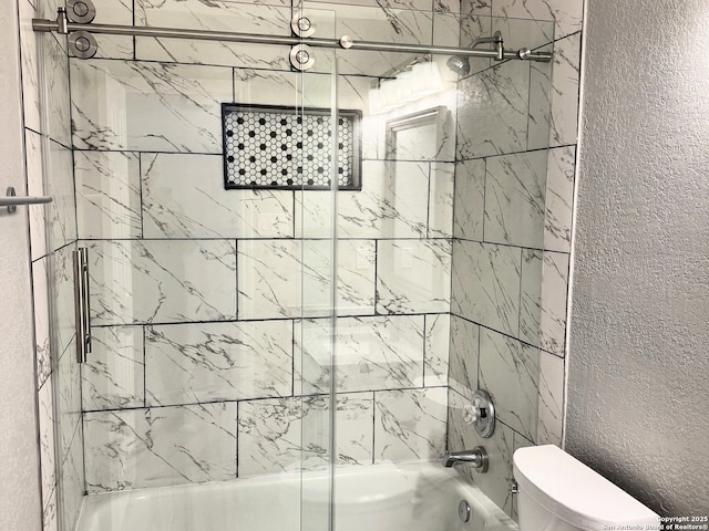 full bathroom with combined bath / shower with glass door, toilet, and a textured wall