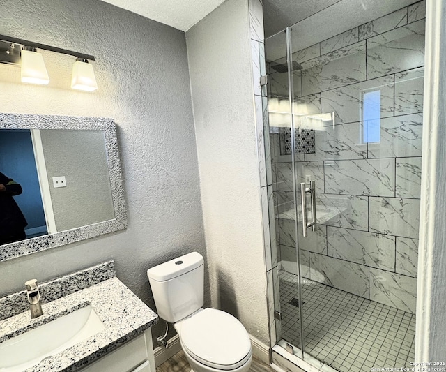 full bath featuring vanity, a shower stall, toilet, and a textured wall