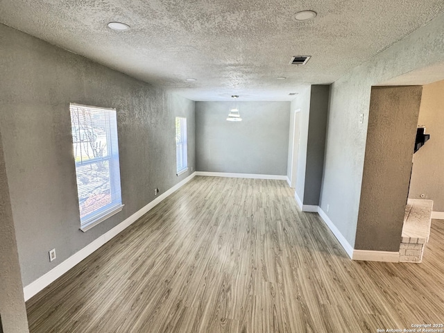 unfurnished room with visible vents, baseboards, a textured ceiling, and wood finished floors