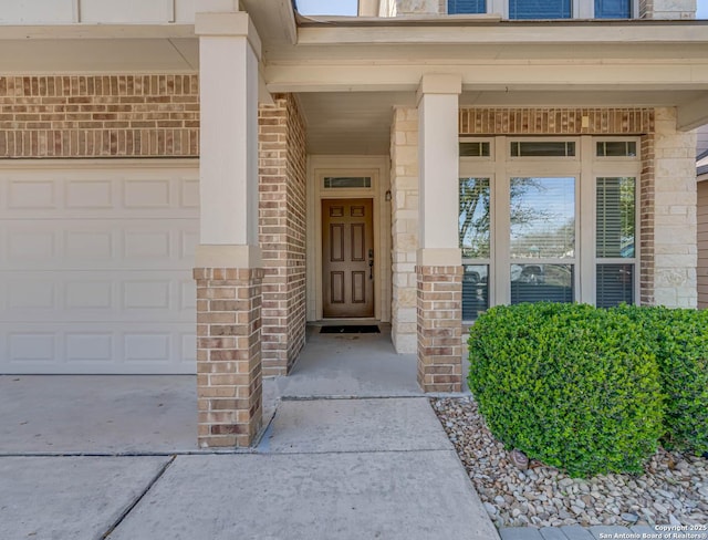 entrance to property featuring driveway, a garage, brick siding, and stone siding