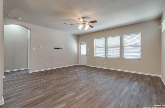 unfurnished room with wood finished floors, visible vents, arched walkways, ceiling fan, and a textured ceiling