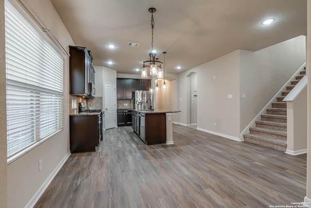 kitchen with visible vents, decorative backsplash, appliances with stainless steel finishes, arched walkways, and a kitchen island with sink