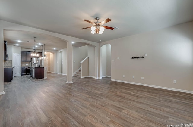 unfurnished living room with arched walkways, ceiling fan, and wood finished floors