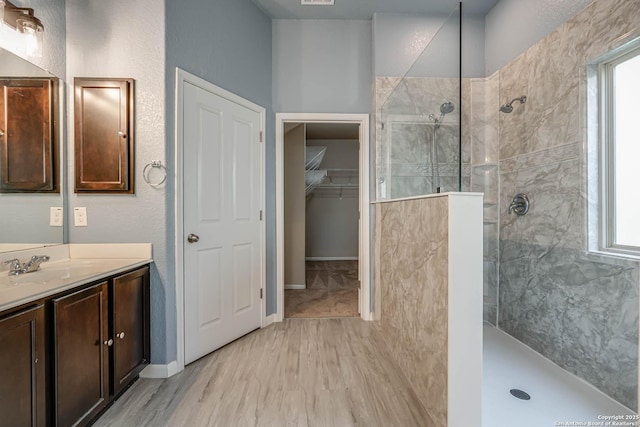 full bath featuring a walk in shower, vanity, a walk in closet, and wood finished floors